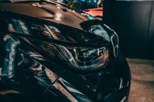 Close-up of a shiny black car's headlight in Munich, highlighting design and elegance.