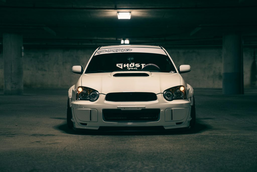 pexels photo 27703409 27703409 A sleek white sports car with modifications parked in a dimly lit industrial garage.