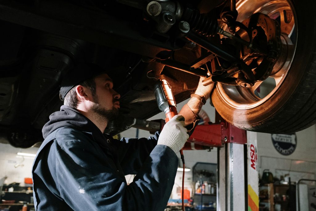 pexels photo 4489749 4489749 Mechanic examining car's undercarriage at a garage, focusing on vehicle maintenance.